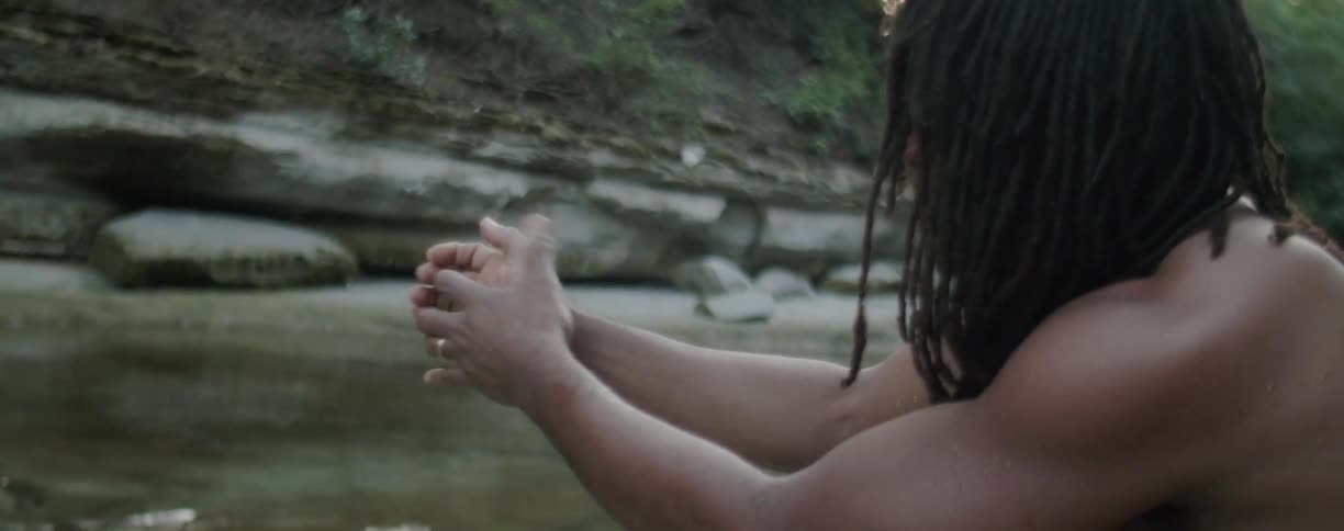 Man sits at the edge of a stream flexing his hand