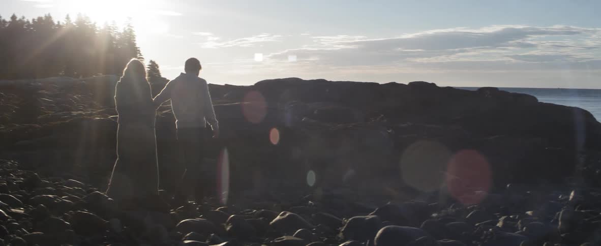 A man and a woman holding hands and walking across rocks