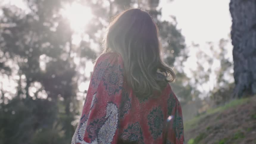 Woman walks beneath tall trees