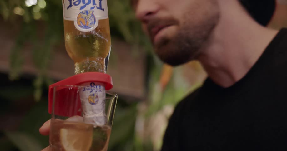 Man drinks from a straw as a beer bottle is upside down in his glass