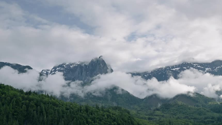 Clouds pass above and through the snowy mountains - 4K Aerial