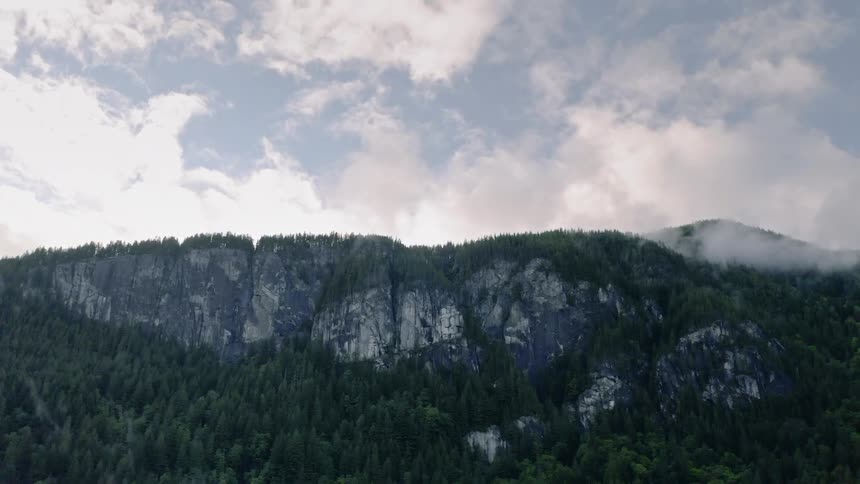 Clouds float above mountains and pine trees - 4K Aerial