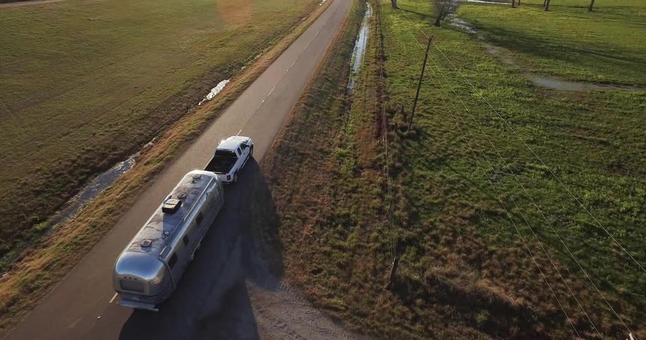 Truck pulls a trailer on a rural road at sunset