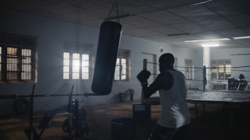 A man in a gym wearing boxing gloves punches a punching bag