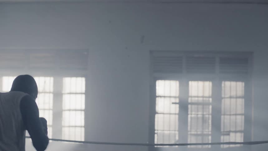 A boxer is shadow boxing inside a gym at night