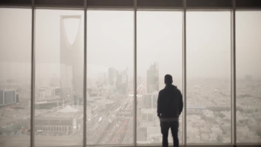 Man stands in a building and looks out the large windows at the city below