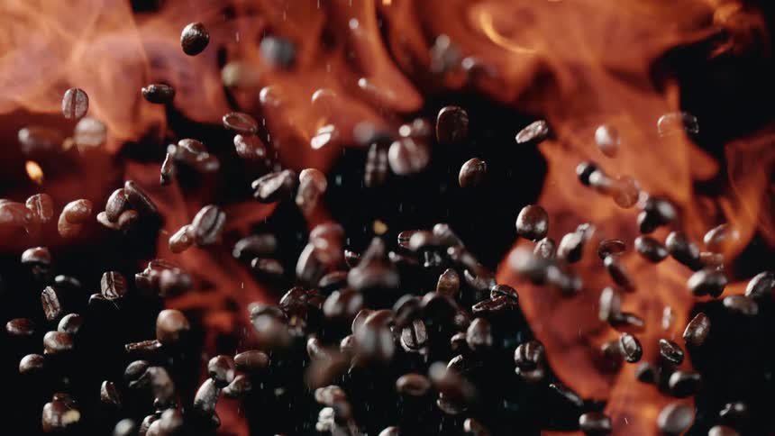 Flames surround the coffee beans as they are tossed into the air