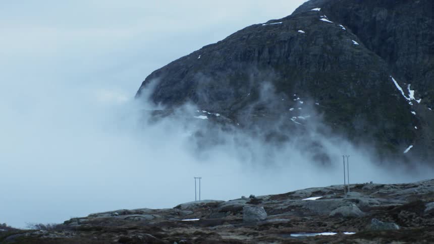 Fog and clouds are drifting over a mountainside in daylight