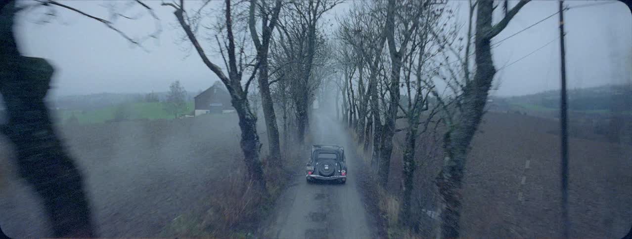 Old car drives along narrow foggy road