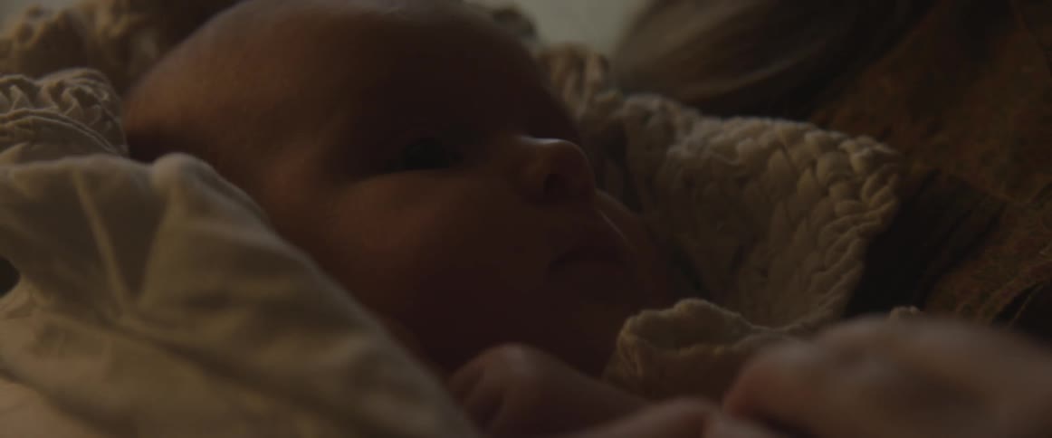 A newborn is swaddled in a blanket and the mother plays with its hands