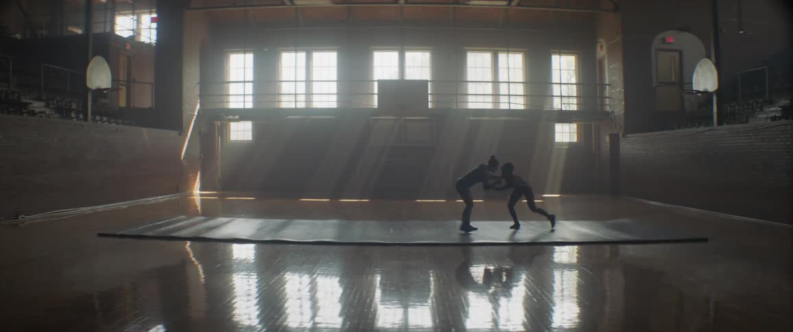Two people wrestle on a mat in a large gym