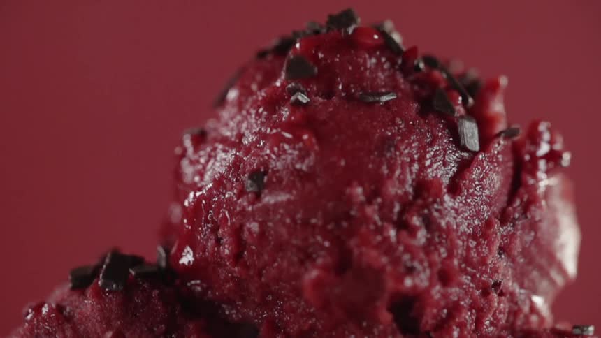Sprinkles fall onto a scoop of red ice cream