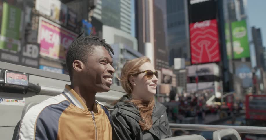 Man and woman sit on top of a bus in the city on a sunny day