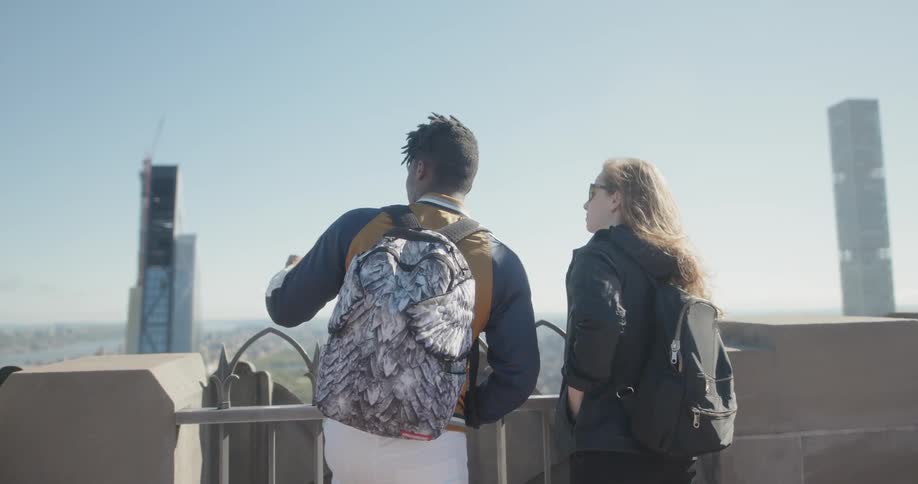 Man and woman stand on a rooftop looking out at a city