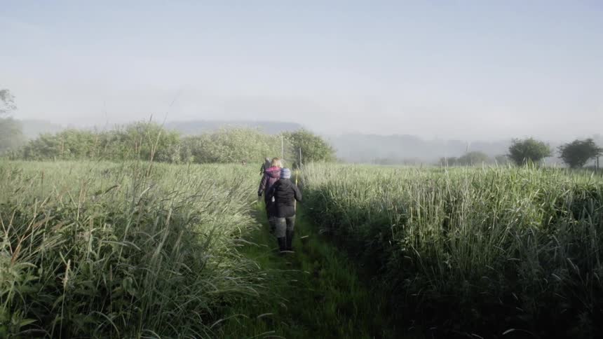 People are hiking on a small path through the very tall grass