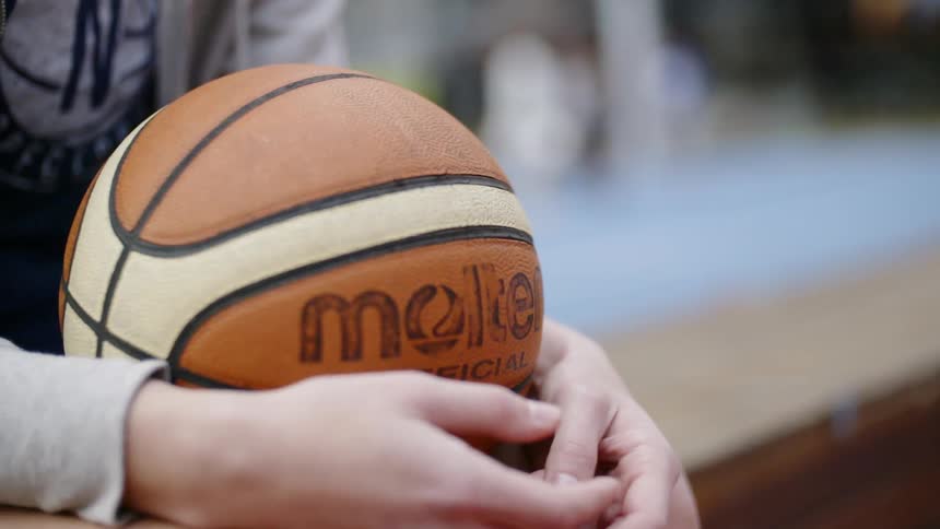 A person sits down holding a basketball in their lap