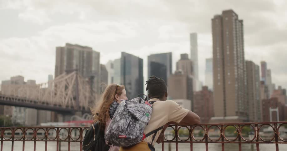 Two people lean on the railing facing the city