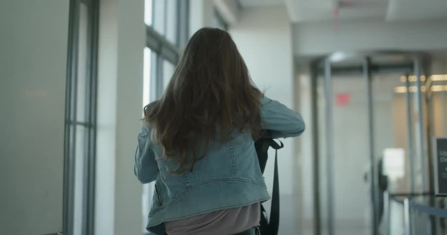 Woman walks along hallway looks through backpack