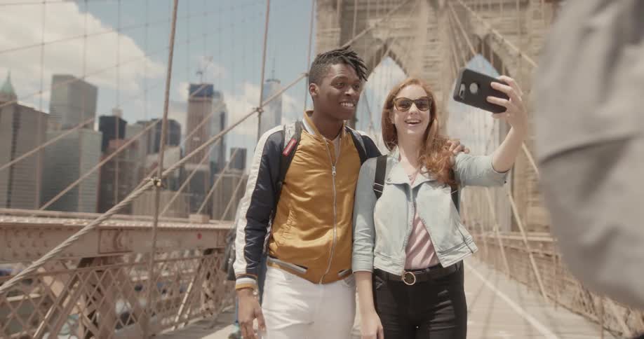 Man and woman smile and take a picture of themselves standing on a bridge in a city