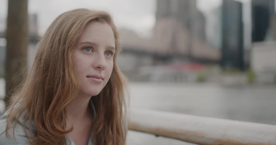 A girl looks down by the water near the city