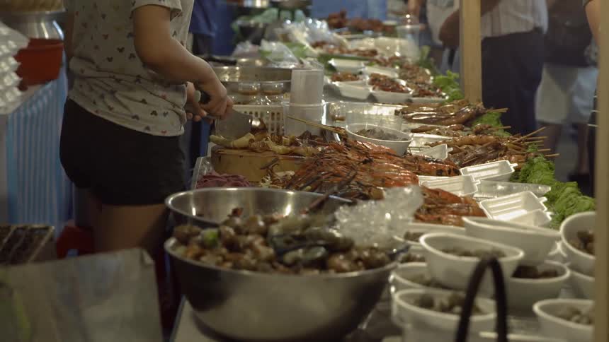 Person carves meat at a crowded banquet table in a market at night