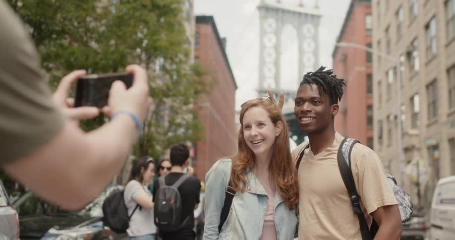 A couple poses for a photo in a city and the man holds up bunny ears