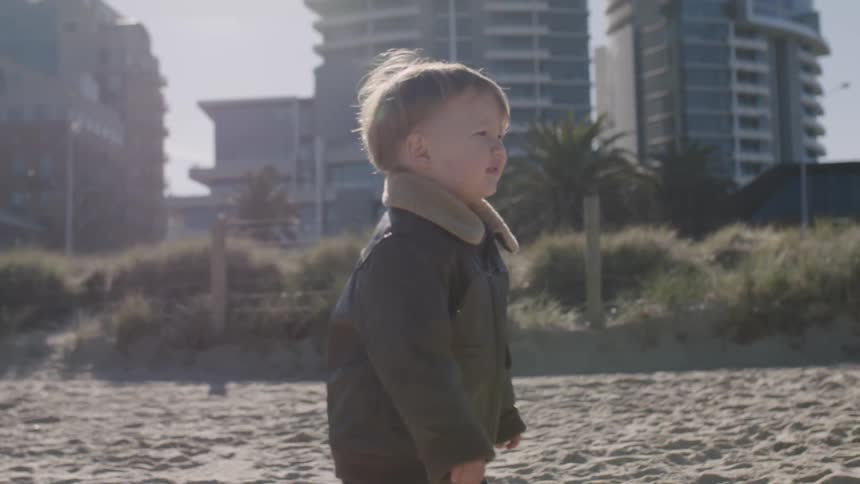 A boy wearing a jacket walks on the sand on a sunny day