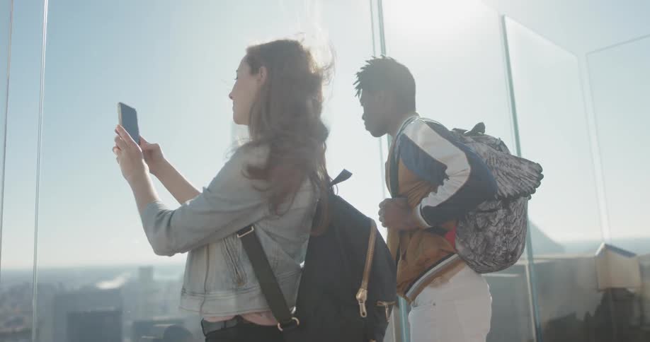 A woman takes a photo with her phone through the glass of a sky walk above the city