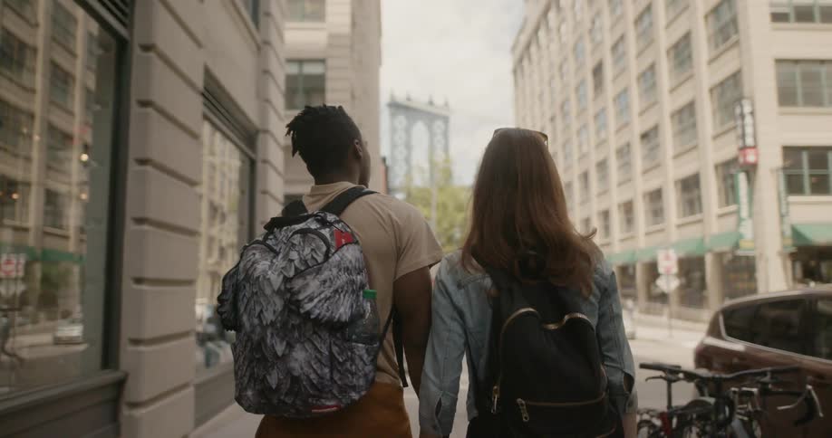 A man and woman walk in the city wearing backpacks