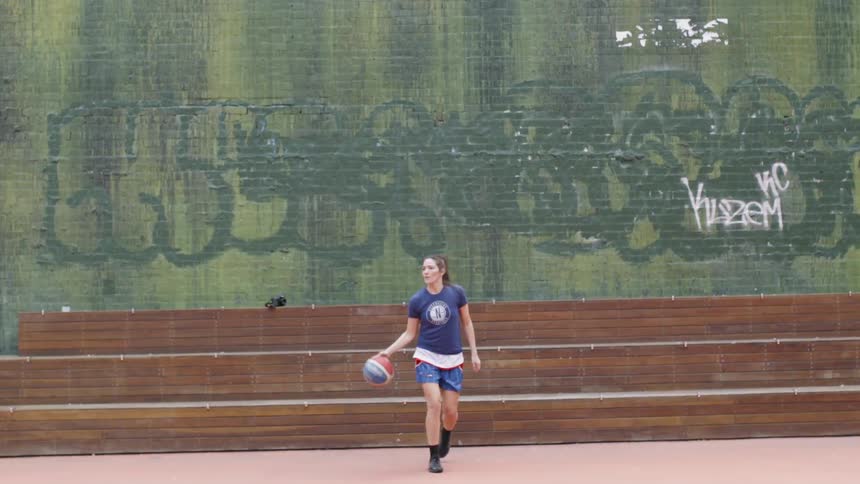 A woman sitting on the bleachers gets up with the basketball