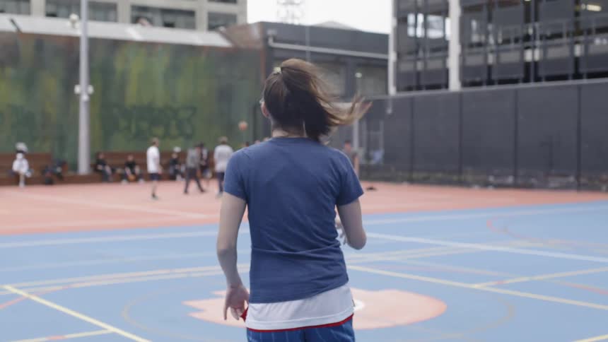 A woman walks on the basketball court dribbling a ball