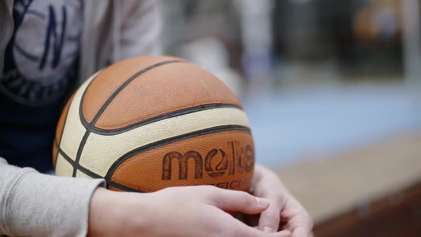 A person holds a basketball as they sit down