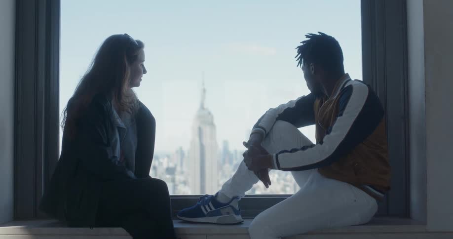 A man and woman sit on the windowsill talking