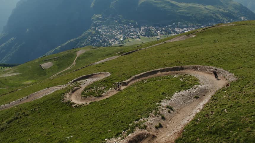 Mountain bikers descend a green slope down a curvy road