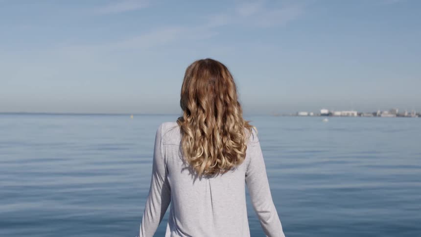 A woman leans against a railing and looks out at the water
