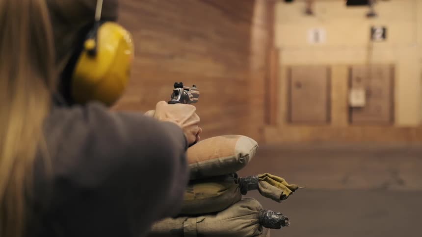 A woman aims and fires a handgun at an indoor shooting range