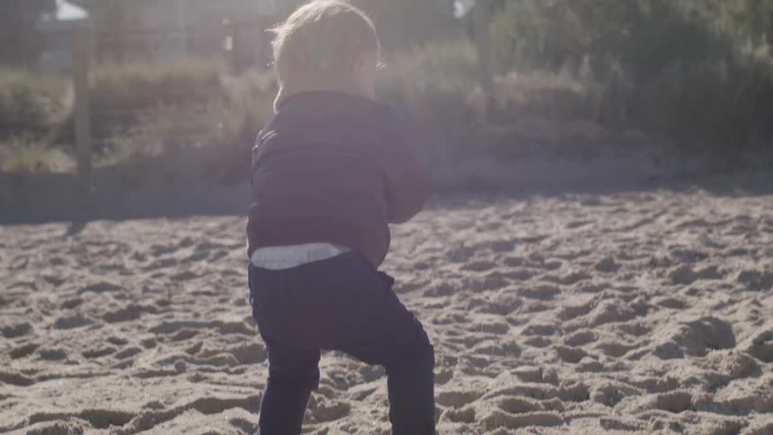 A child falls while walking in the sand on a beach