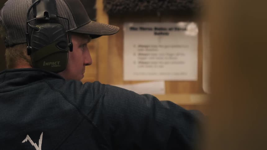 A man fires a gun wearing ear muffs in the gun range