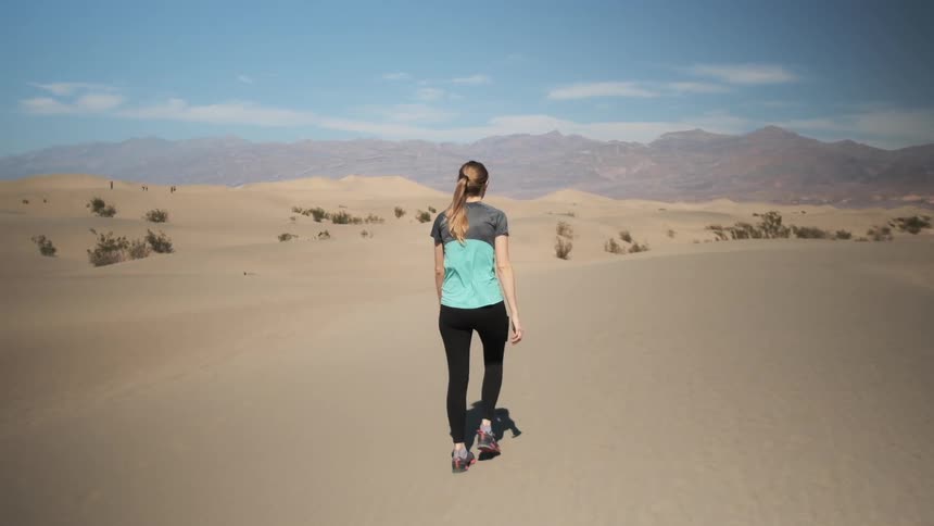 A woman walks through the desert on a very sunny day