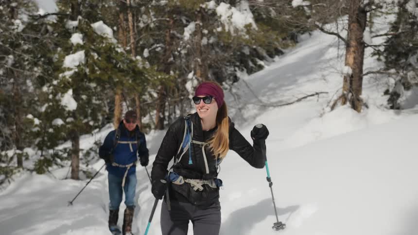 Man and woman smile as they hike up a snowy mountain
