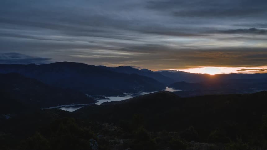 The sun sets behind a mountain as waves flow across the sky