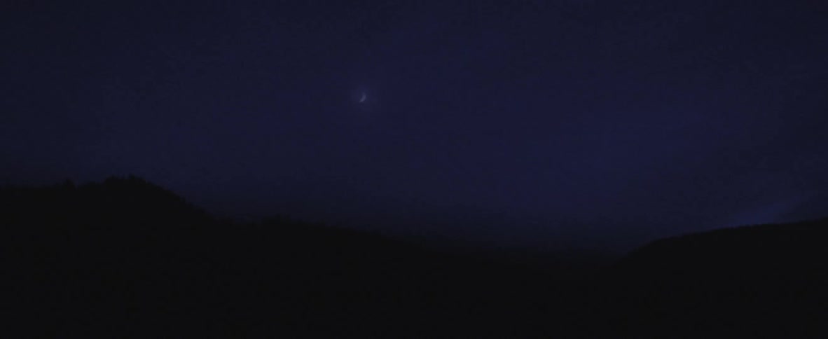 A crescent moon in the night sky over a natural landscape