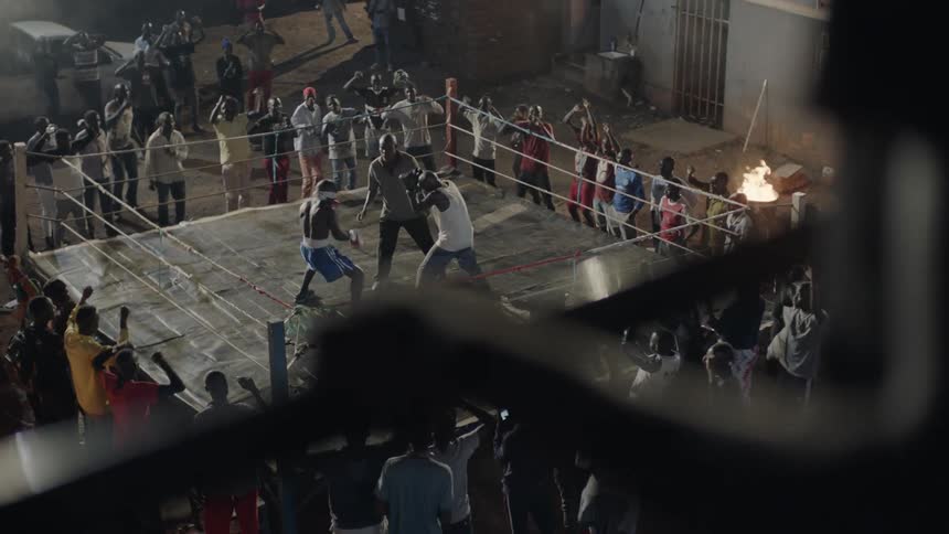 Two boxers are fighting in a ring outside at night