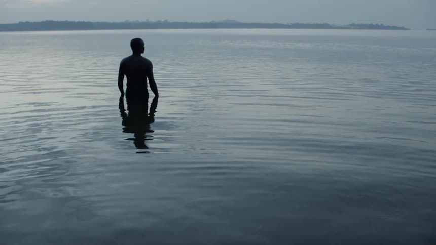 A man stands in a lake at sunset