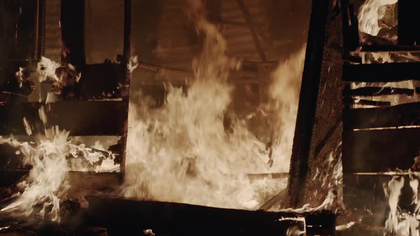 A fire is destroying a wood structure at night