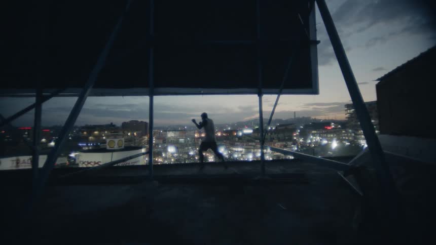 A boxer punches the air on a building rooftop at dusk