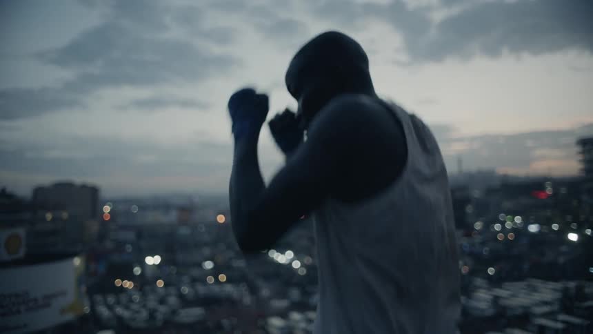 Man practices punching while standing on a rooftop overlooking a city