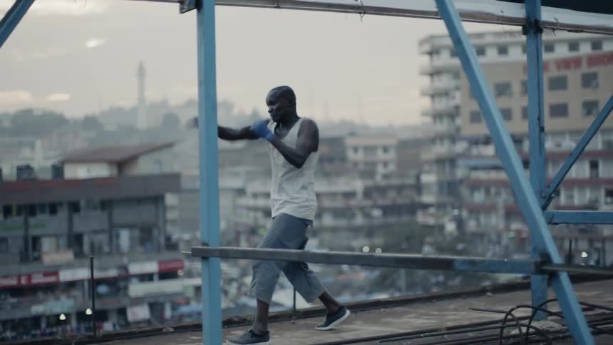 A boxer is shadow boxing on a rooftop at sunset