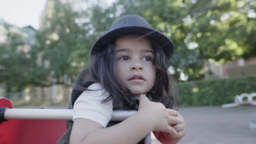 A young child sitting thoughtfully on a spring rocker at park playground.