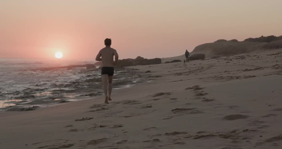 A man jogs on a beach at sunset
